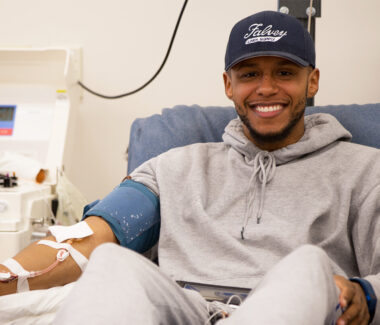 Smiling young man in a baseball cap donating blood at a Rhode Island Blood Center location.