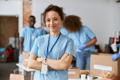 A Rhode Island Blood Center volunteer standing in a blue shirt with her arms crossed smiling at a blood drive.