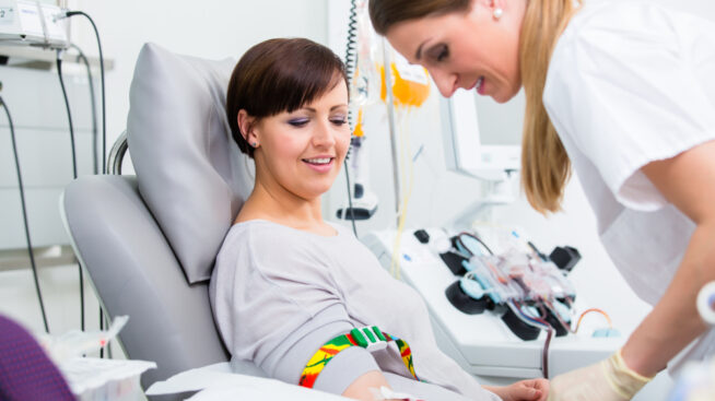 Female phlebotomist taking blood from a female blood donor reclining in a donation chair.